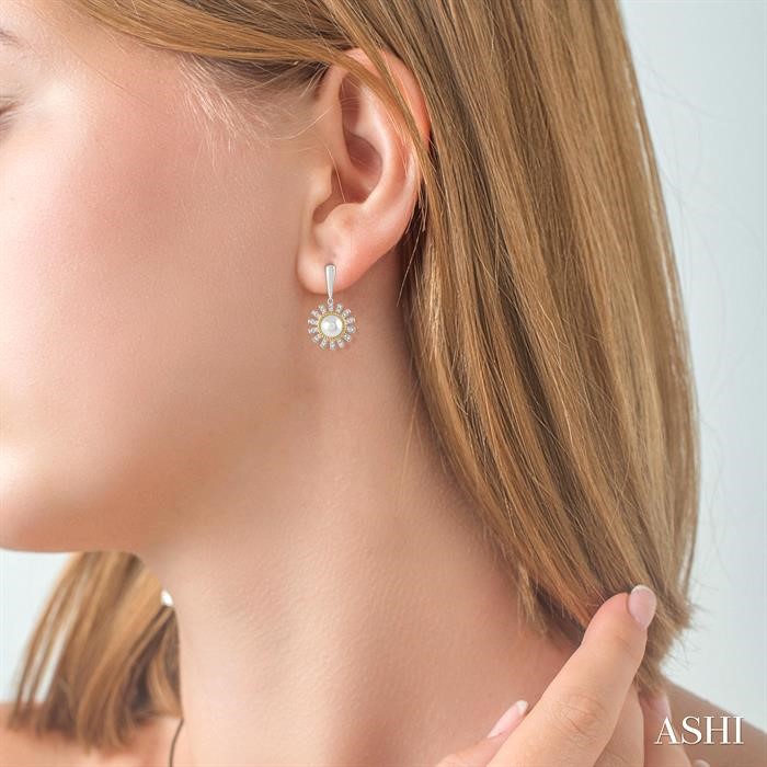 Blonde woman wearing sunflower-shaped pearl and diamond earrings by Ashi, available at Deutsch Fine Jewelry in Houston, TX.