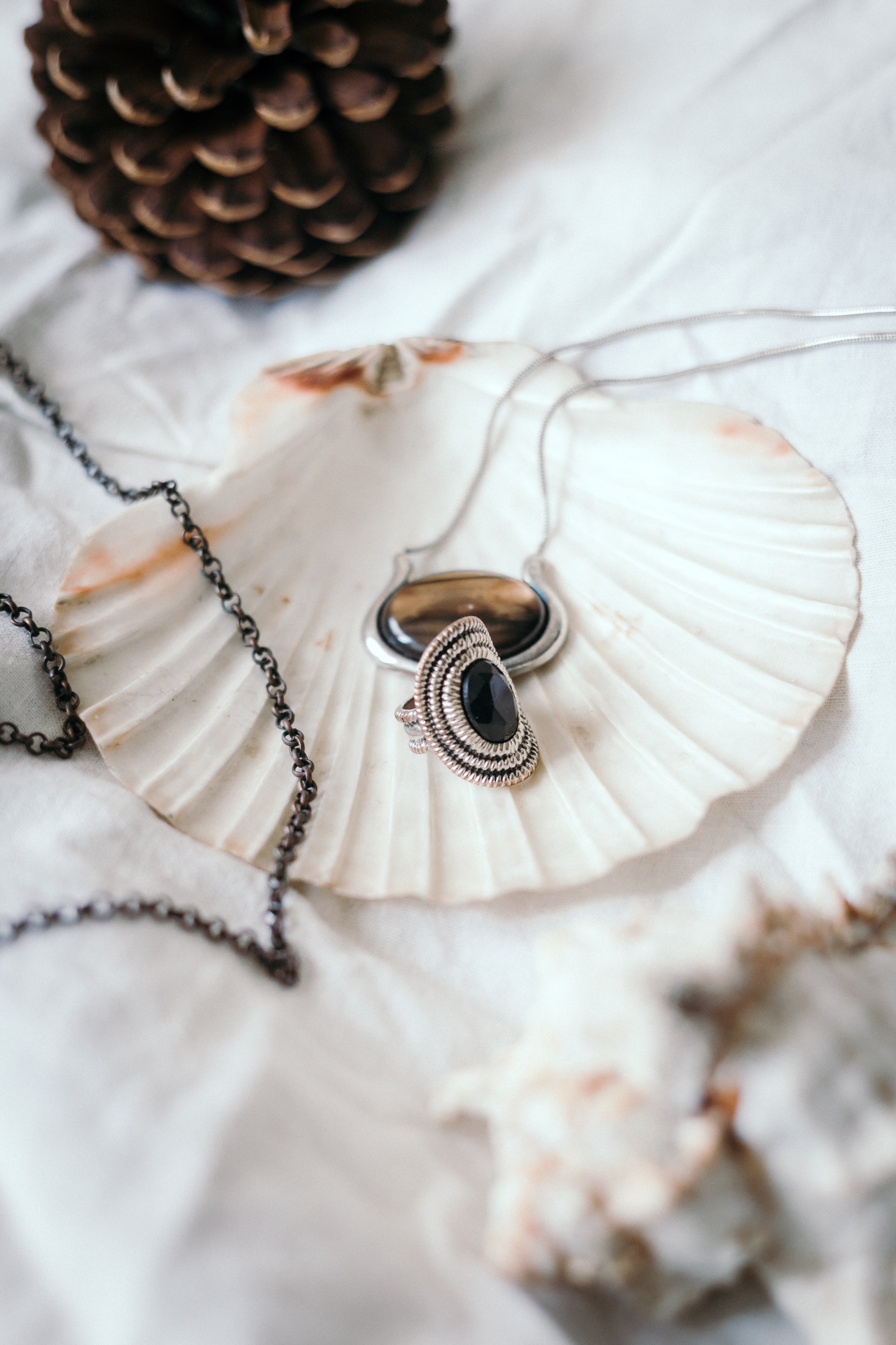 A cabochon gemstone pendant and a cabochon gemstone ring rest on a seashell on a white tablecloth - photo by Jakub Tabisz via Pexels