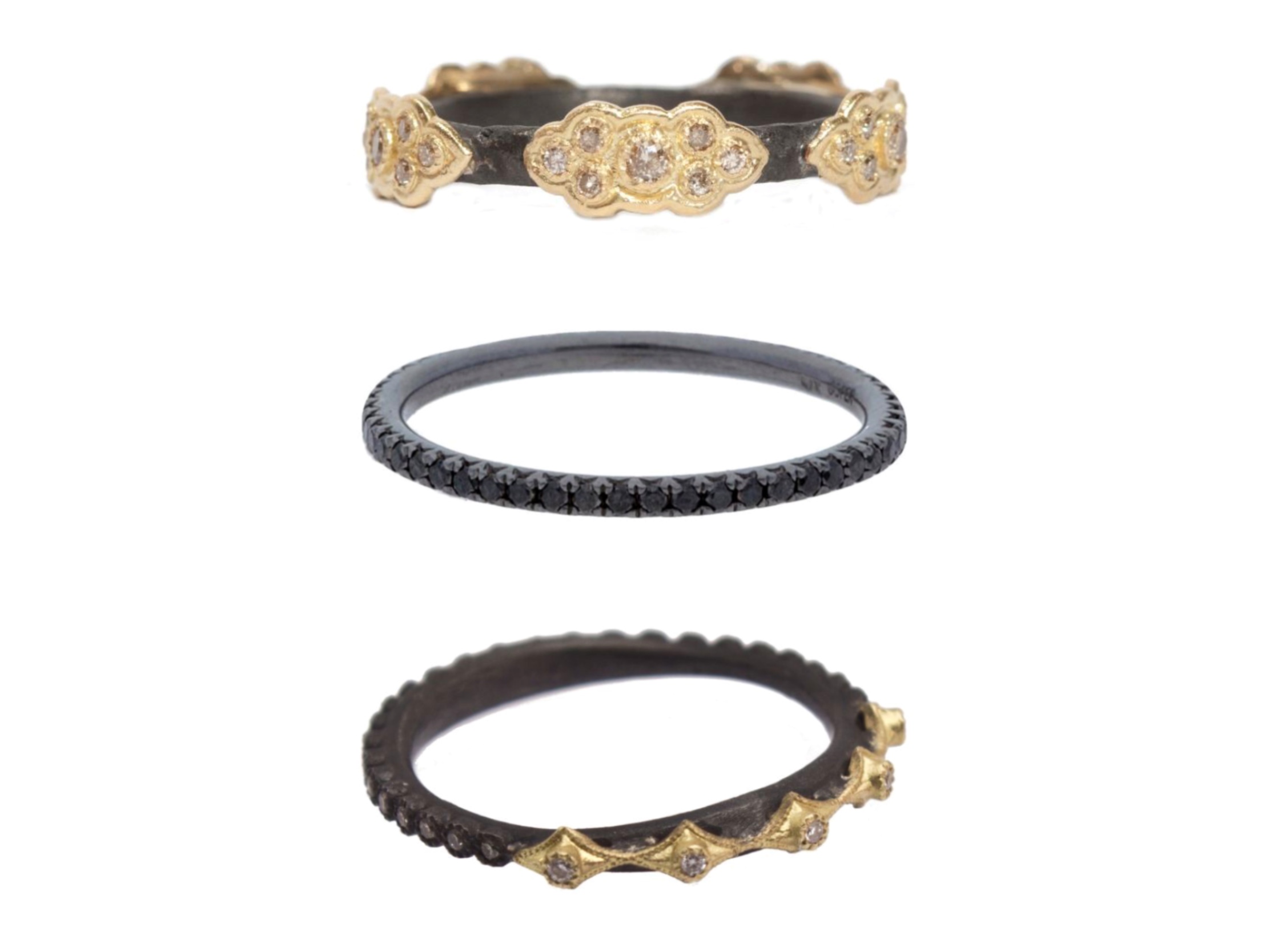 A stack of rings with darkened metal and patina. The bottom ring is the Old World Stack Band Ring With White And Champagne Diamond Crivelli Stations by Armenta, the center ring is Black Diamond Stackable Ring by Deutsch Signature, and the top band is the Old World Stack Band Ring With Champagne Diamond Scrolls by Armenta. All are available at Deutsch Fine Jewelry in Houston, Texas.