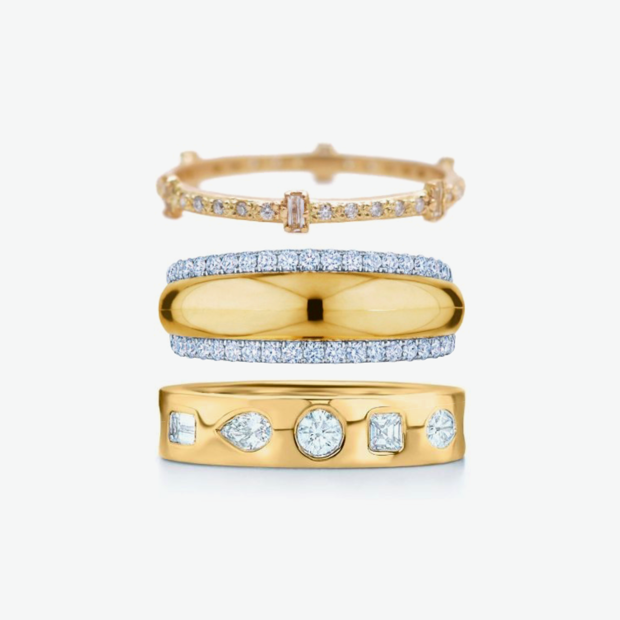 The top ring is the Baguette Stack Band by Armenta: a thin yellow gold band encircled with tiny white diamonds and stationed with solitary baguette-cut white diamonds. The middle ring is the yellow gold Orbit Domed Ring by Kwiat with white diamond pave on either side. The Bottom ring is the yellow gold Stackable Ring with Fancy Shape Diamonds which are set inlaid across the facing band. All three rings are available at Deutsch Fine Jewelry in Houston, Texas.
